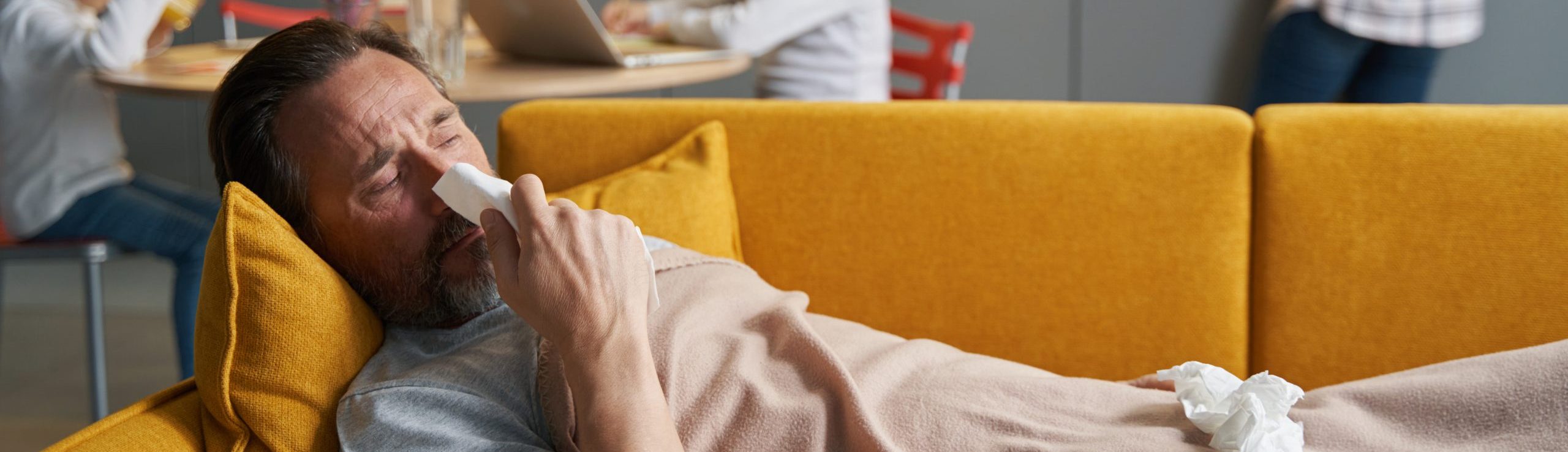 Sick man lying on sofa in kitchen and wiping his nose